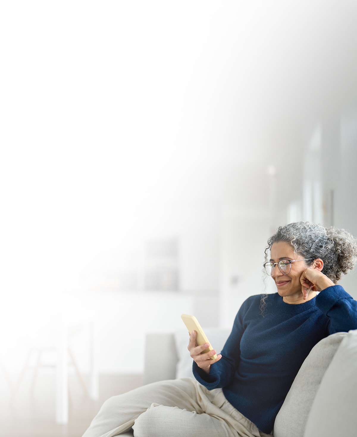 Une femme propriétaire, assise sur un canapé et regardant son téléphone en souriant.