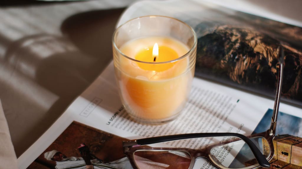 Perfumed candle lit, magazine and reading glasses on bed and pillows