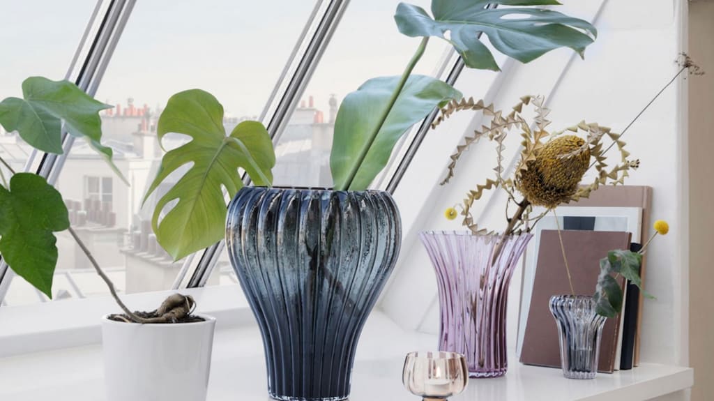 Vases en verre coloré sur le bord d'une grande fenêtre avec vue sur ville, plantes vertes à grandes feuilles