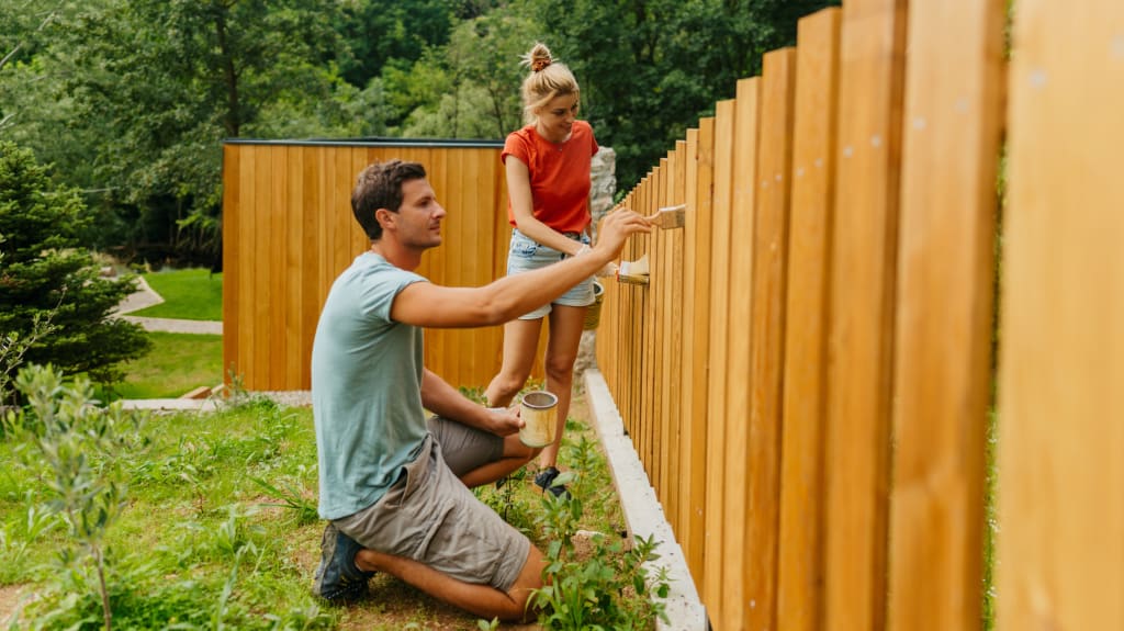 A man and a woman painting a fence
