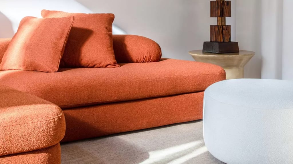 Canapé orange brûlé en laine bouclée avec grands coussins, pouf rond blanc ivoire, table avec lampe en bois