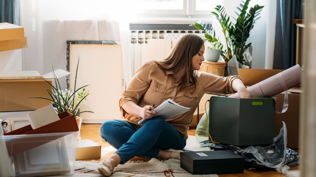 Femme assise sur le sol, entourée d'articles et préparant son déménagement