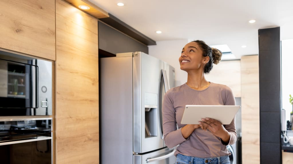 Femme souriante qui règle les luminaires de sa cuisine à l’aide d’un système automatisé sur une tablette