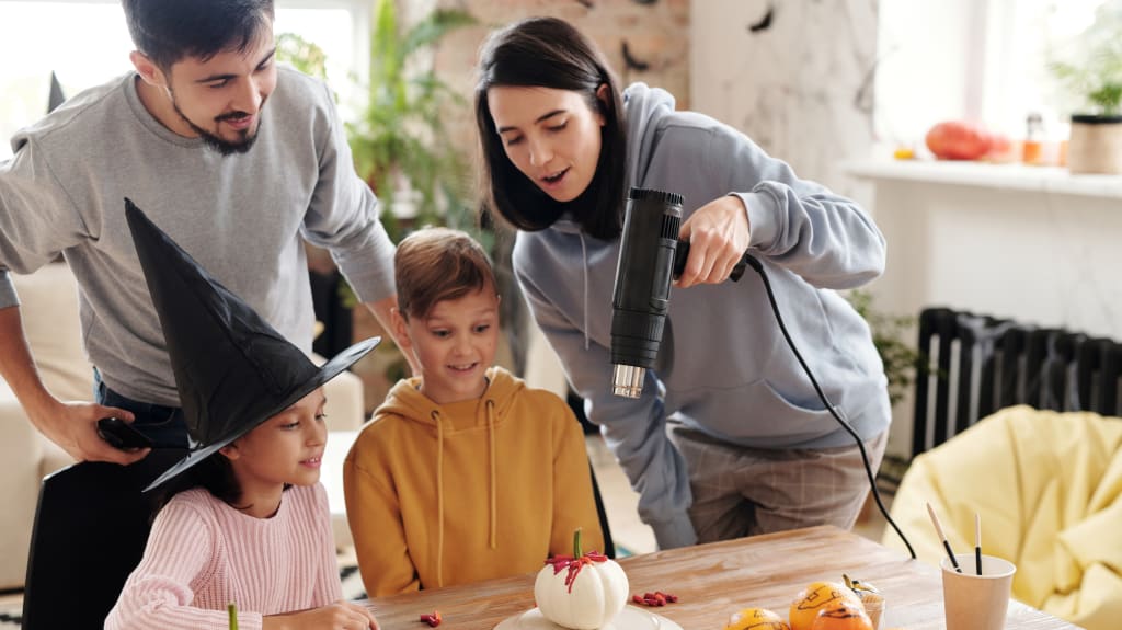 Famille de deux adultes et deux enfants regardant une citrouille d’Halloween peinte en blanc