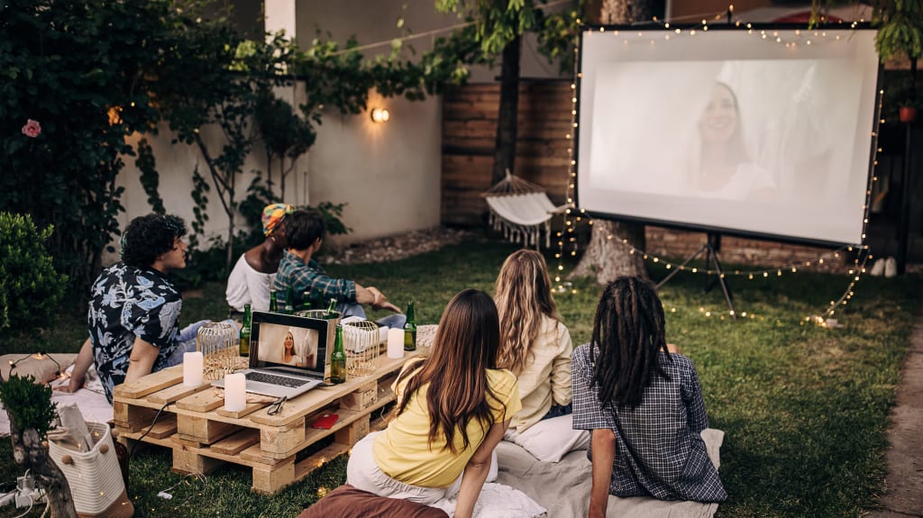Young adults watching a movie on a projector screen in a backyard