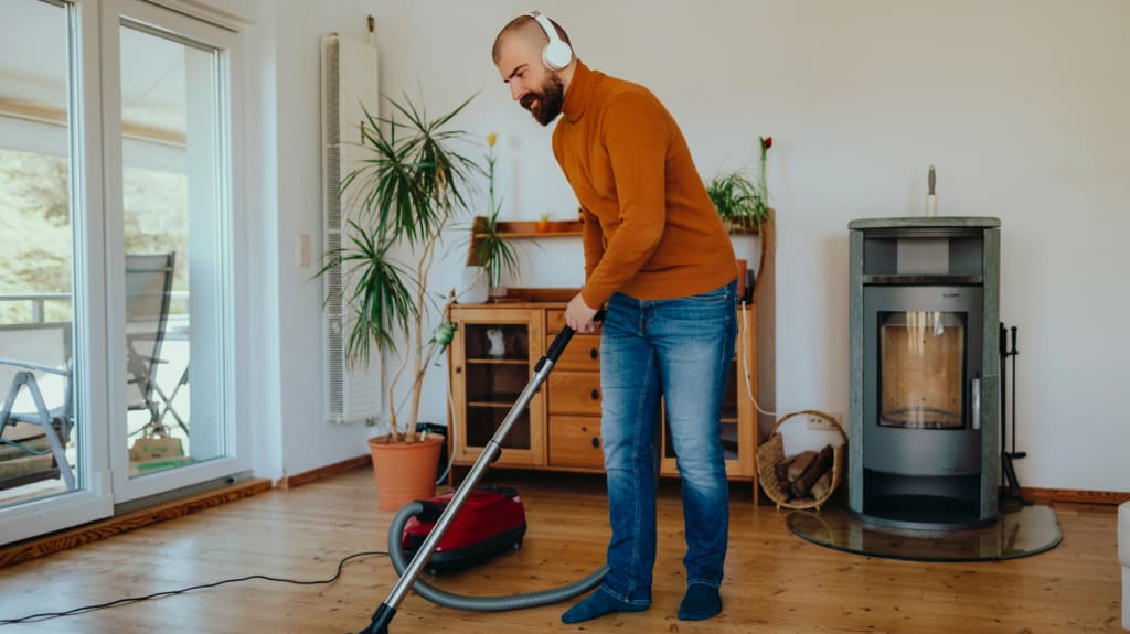 Homme avec écouteurs sur les oreilles passant la balayeuse sur plancher de bois franc de salon