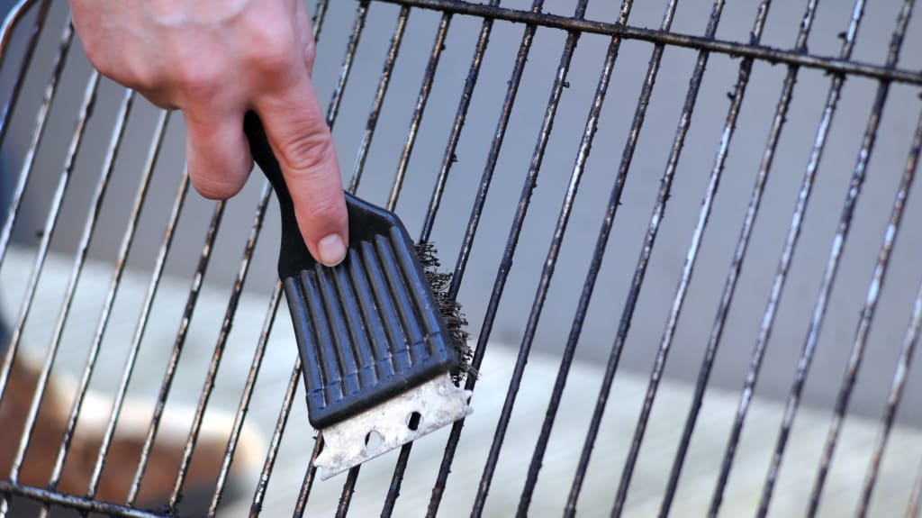 Hand of a person brushing a BBQ grill to clean it