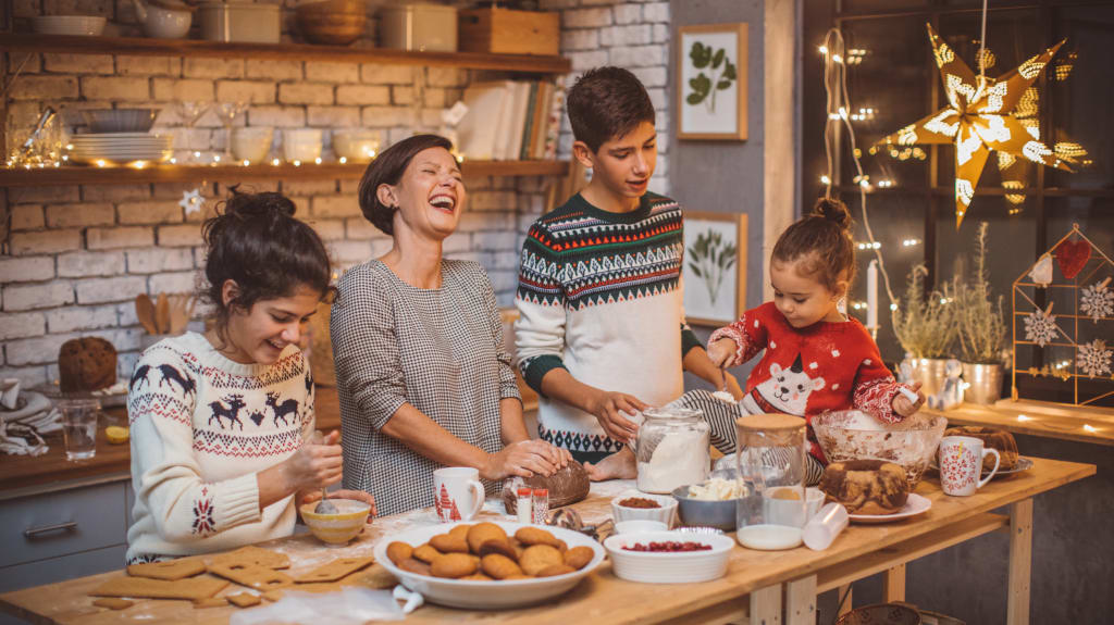 Famille de quatre personnes dans un décor du temps des Fêtes en train de préparer et de décor des petits gâteaux