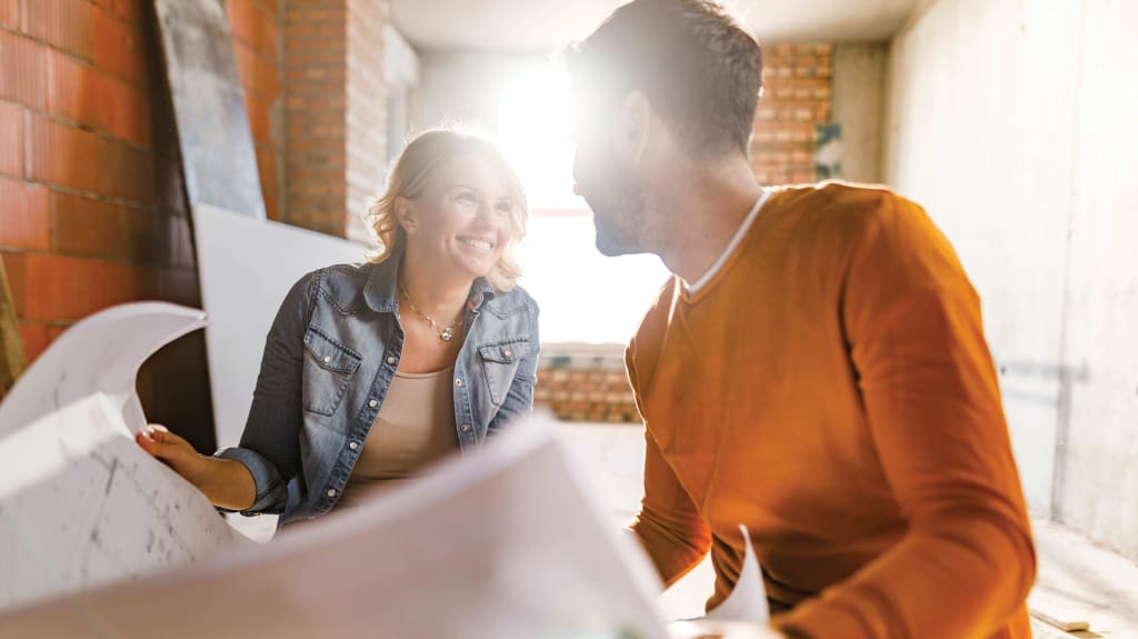 Couple smiling at each other with a renovation project plan in hand