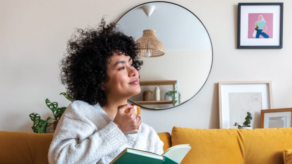 Femme assise sur canapé jaune avec mur décoré d'un miroir rond et de cadres dans une pièce lumineuse