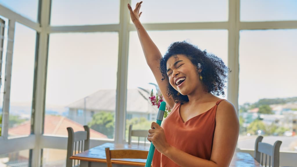 A woman holding a mop and raising her hand while listening to music