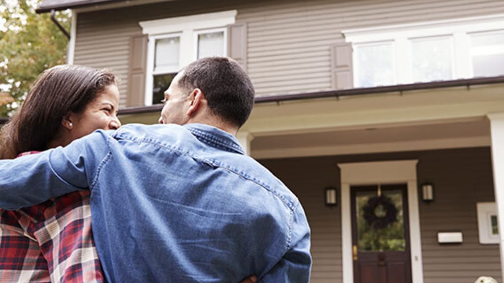 Couple embracing and looking at each other affectionately in front of a cottage after successfully selling their house in a buyer's market