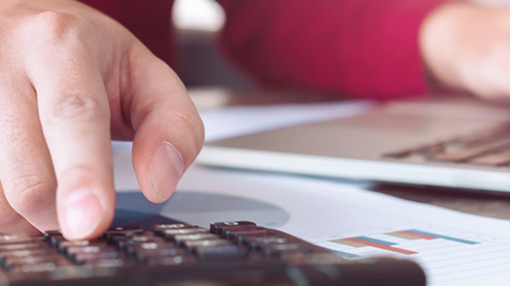 Person with one hand on a calculator and the other on a laptop keyboard to determine the loan amount for a property