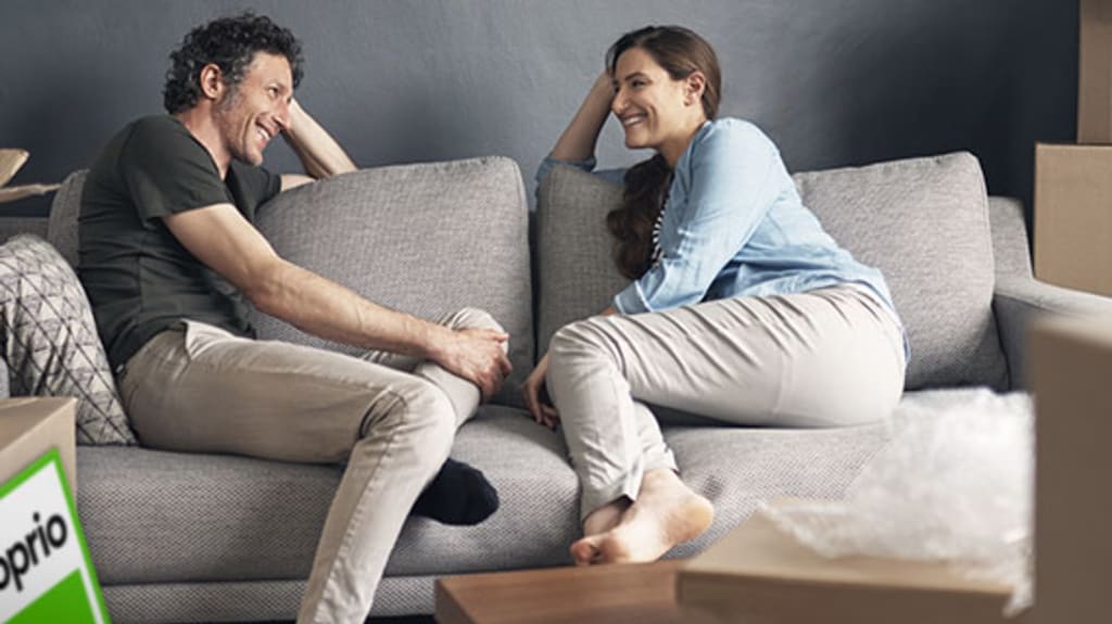 Couple sur un divan avec des boîtes de déménagement et une pancarte DuProprio