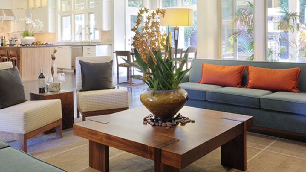 Salon incluant une table basse en bois, de longs divans gris et deux fauteuils blancs garnis de coussins décoratifs dans une propriété à vendre