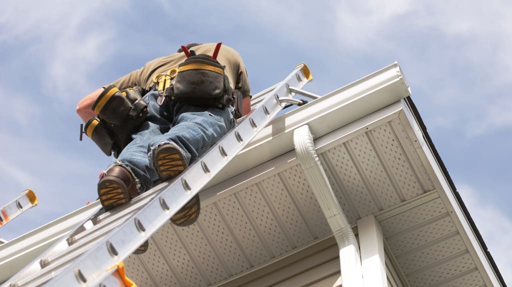 Homme grimpé dans une échelle inspecte la toiture d'une maison