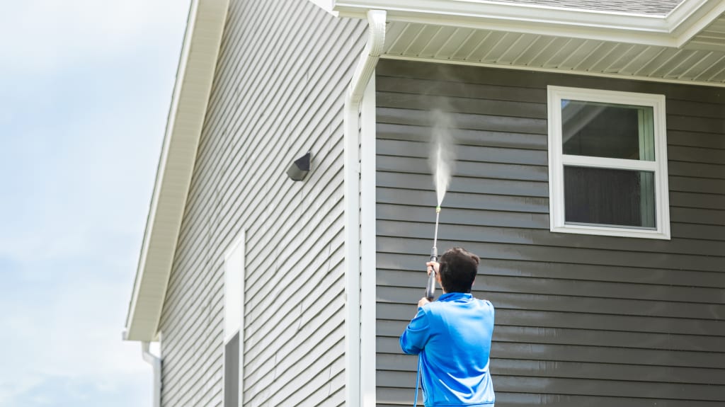 Homme en t-shirt bleu nettoie le revêtement extérieur de la maison avec une machine à pression