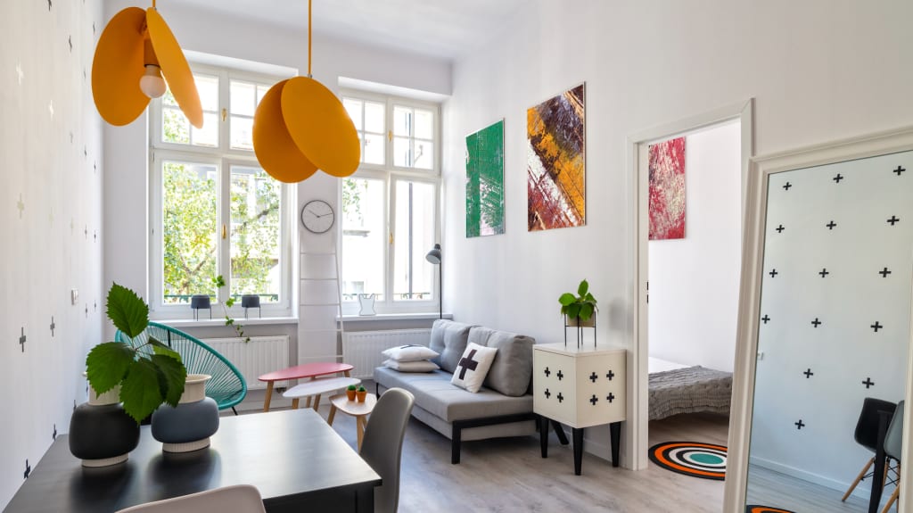 Appartement de couleur blanche, des fenêtres en bois, un canapé gris et des accessoires colorés