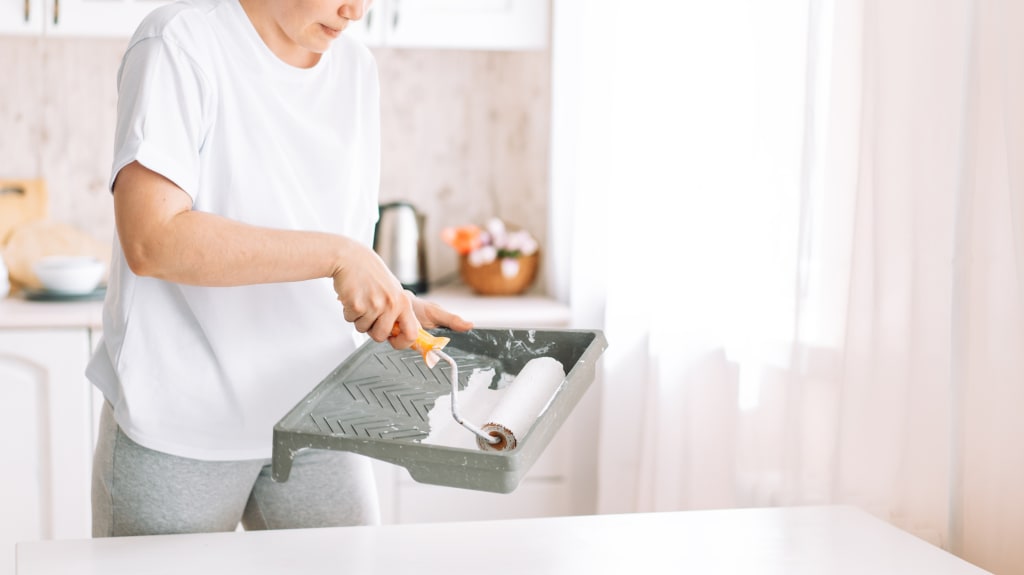 Person using a tub and roller of white melamine paint to paint the kitchen countertop