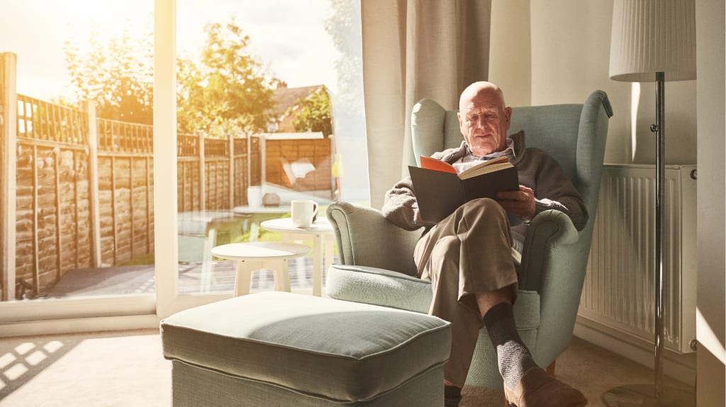 Homme âgé assis dans un fauteuil lisant un livre à la maison