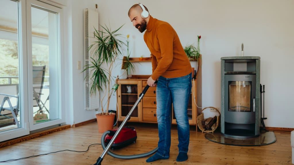 Man with headphones vacuuming a hardwood floor in the living room