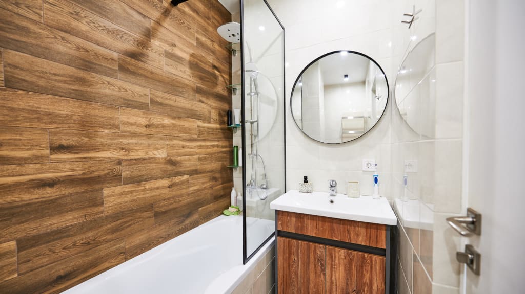Petite salle de bain, incluant une douche baignoire, une vanité en bois et un miroir rond