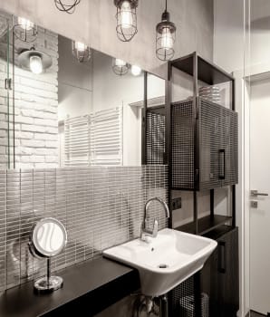 Salle de bain grise avec étagère noire, luminaires suspendus et mur de briques blanches 