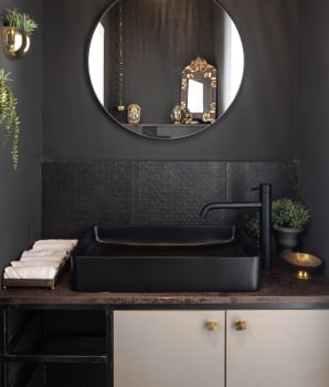 Dark bathroom with black sink, black-framed round mirror and gold hardware