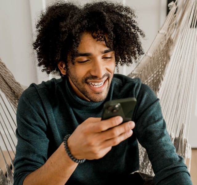 Un homme assis dans une chaise hamac suspendue qui regarde son téléphone