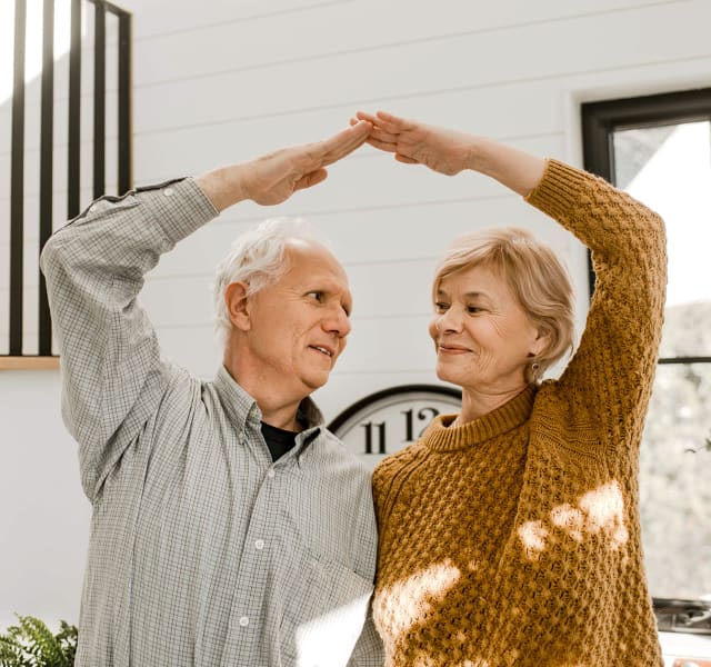 Couple de personnes âgées se tenant par la taille et formant un triangle au-dessus de leurs têtes en joignant leurs bras