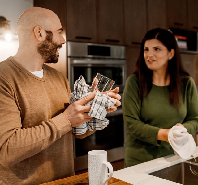 Un couple qui fait la vaisselle. Un homme essuie un verre en discutant avec une femme qui tient un linge à vaisselle