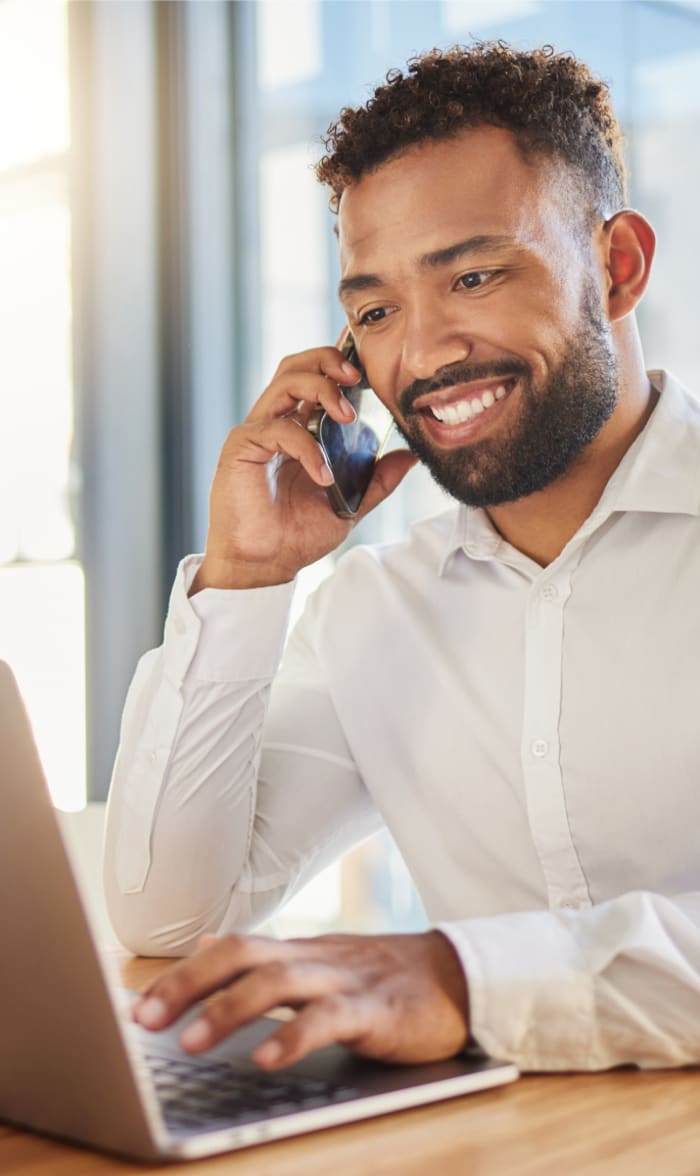 Homme souriant en communication téléphonique, consultant un ordinateur portable