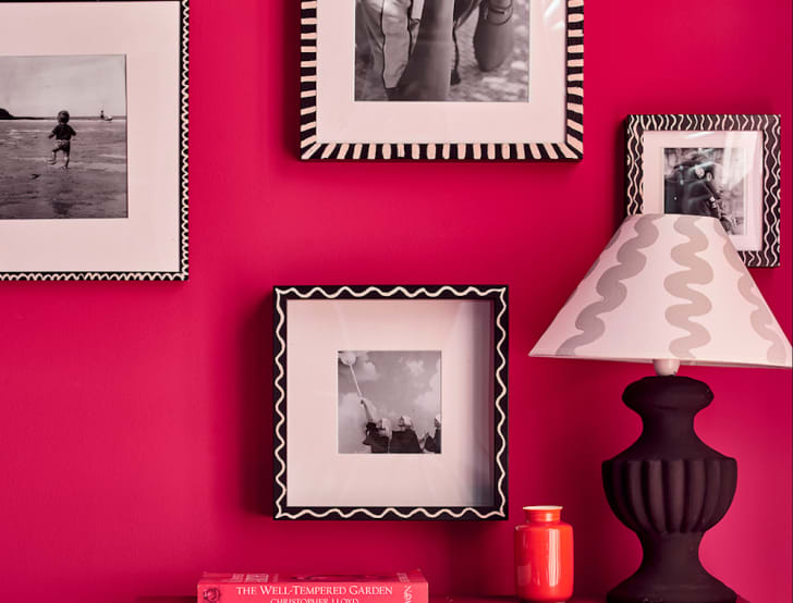 Mur rose framboise, photos noir et blanc encadrées. Lampe, livre et vase sur la table console. 