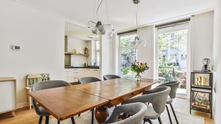 Dining room, open windows on sunny street. Vintage wooden table and chairs with rounded backs. 