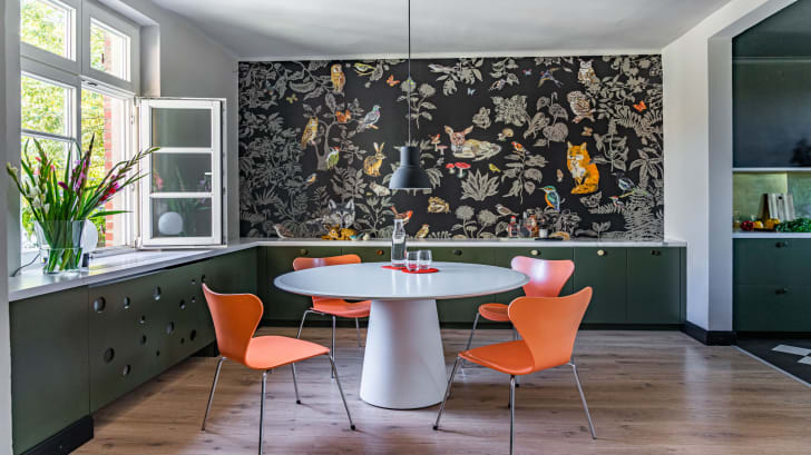 Dining room, vegetal and animal print wallpaper, white table and orange resin chairs. 