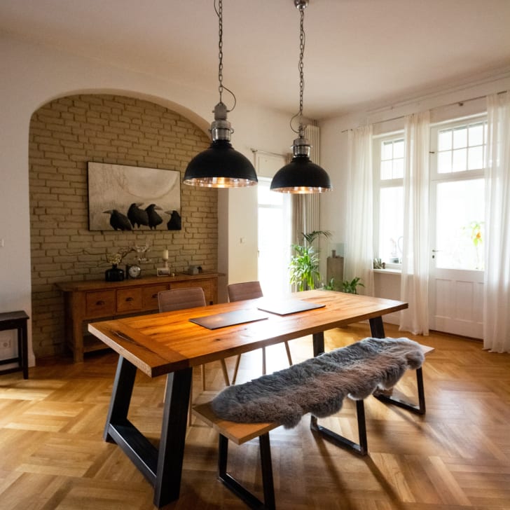 Dining room, brick wall. Wooden table and bench, industrial style suspension light fixtures.