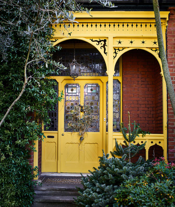 Façade de maison en briques rouges avec porche en bois jaune. Porte double avec vitrail.