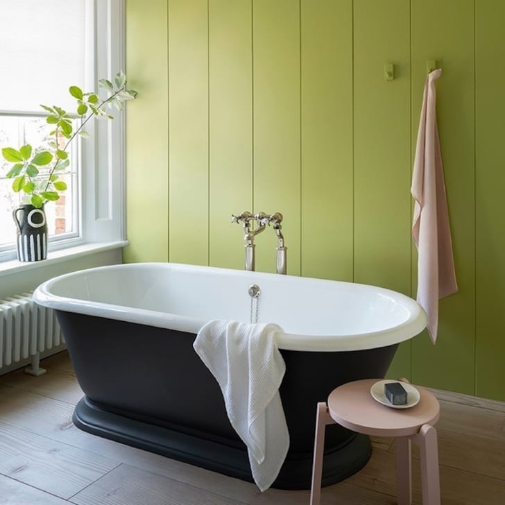Salle de bains, baignoire rétro noire, mur vert laitue, serviette et tabouret rose pâle