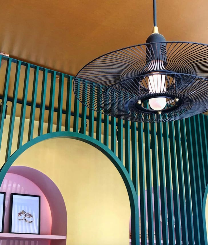 Intérieur de café aux murs colorés jaune et rose, lampe suspendue en grillage de ventilateur noir
