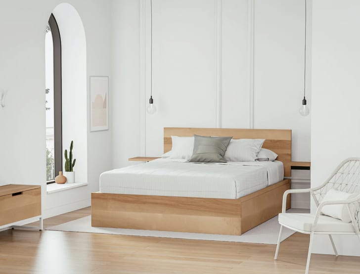 Chambre à coucher, plafond haut, murs blancs, tête et base de lit en bois blond, fenêtre en arche