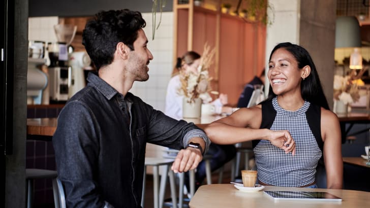 Deux personnes riant et se cognant le coude dans un café