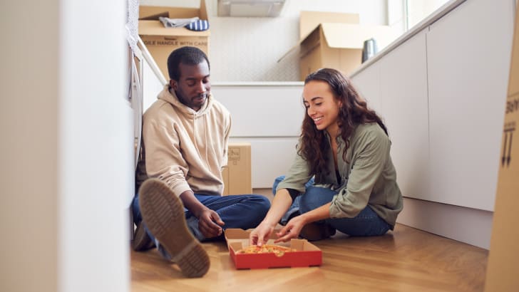 Jeune couple célébrant leur journée de déménagement en mangeant une pizza sur le sol de la cuisine et entouré de boîtes