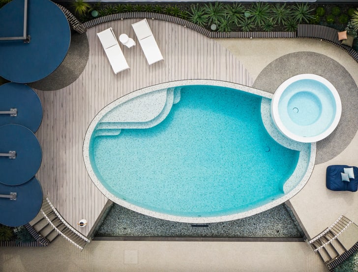 Belle piscine ovale à fond moucheté, spa circulaire à côté, terrasse en lattes de bois