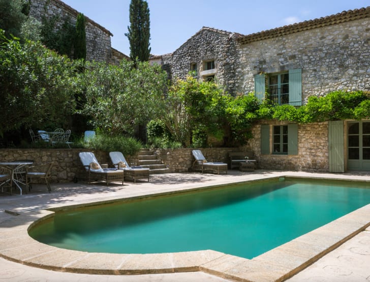 Belles piscines forme rectangulaire avec un côté en arc de cercle, derrière petit hôtel en pierres