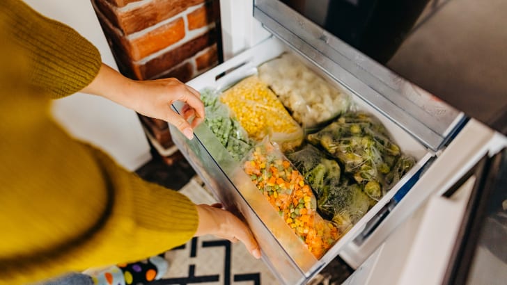 Femme mettant un récipient avec des légumes mélangés surgelés au réfrigérateur