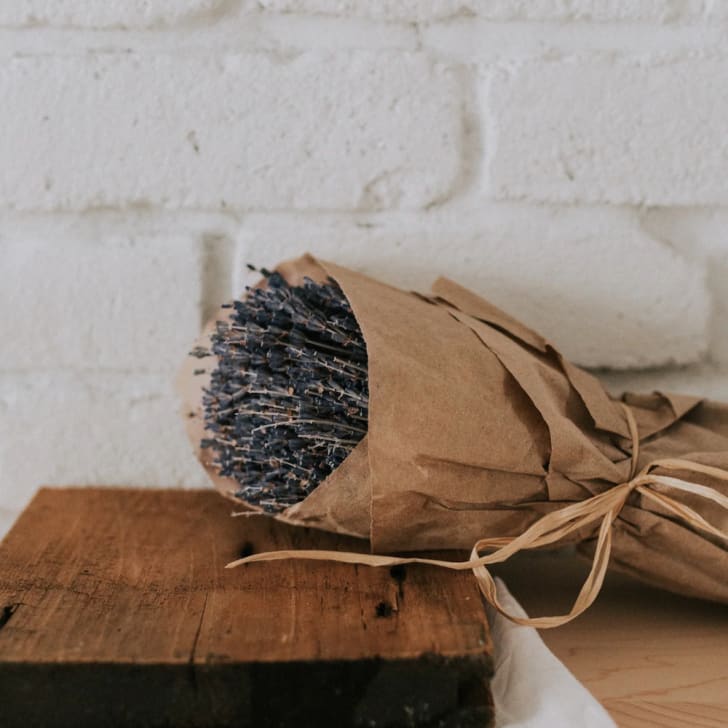 Déco voyage, bouquet de lavande séchée enveloppé dans papier brun avec ruban en raphia, table de bois et mur en briques blanches