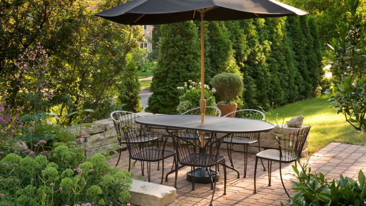 Terrasse pavée avec coin repas extérieur et parasol dans un jardin