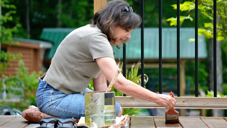 Person staining a deck with a paintbrush