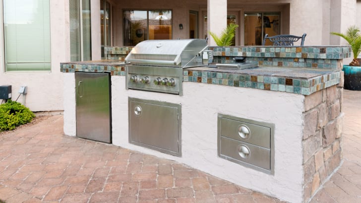 An outdoor kitchen on a paved backyard patio