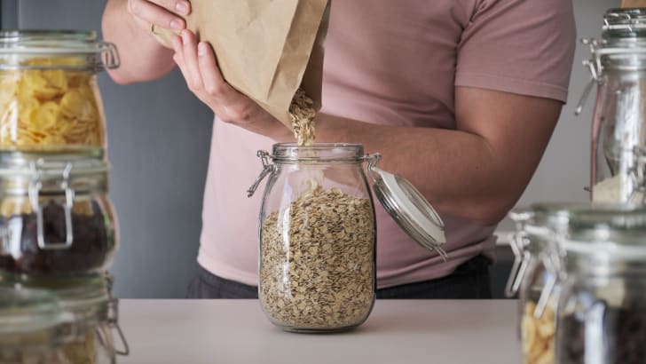 Person pouring oat flakes into a clear storage jar